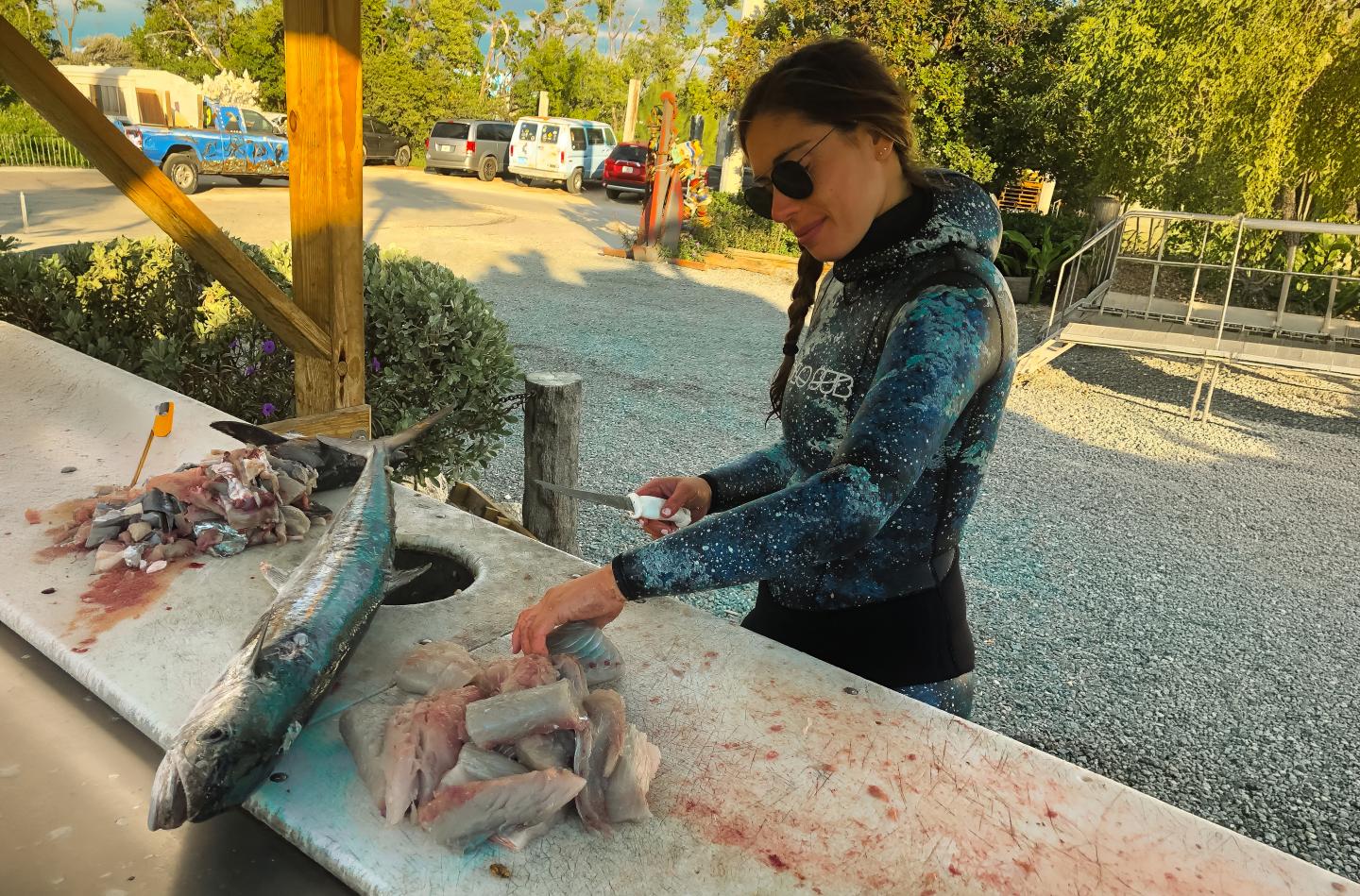 Woman cleaning fish at an outdoor table.
