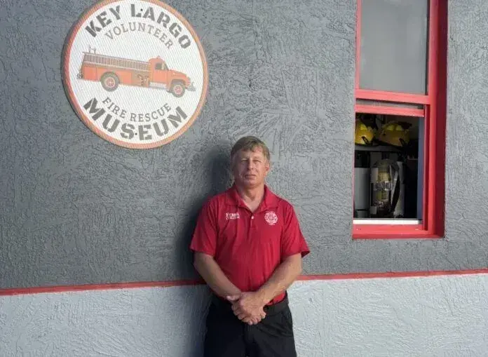 Man in red shirt stands near Key Largo Fire Museum sign.