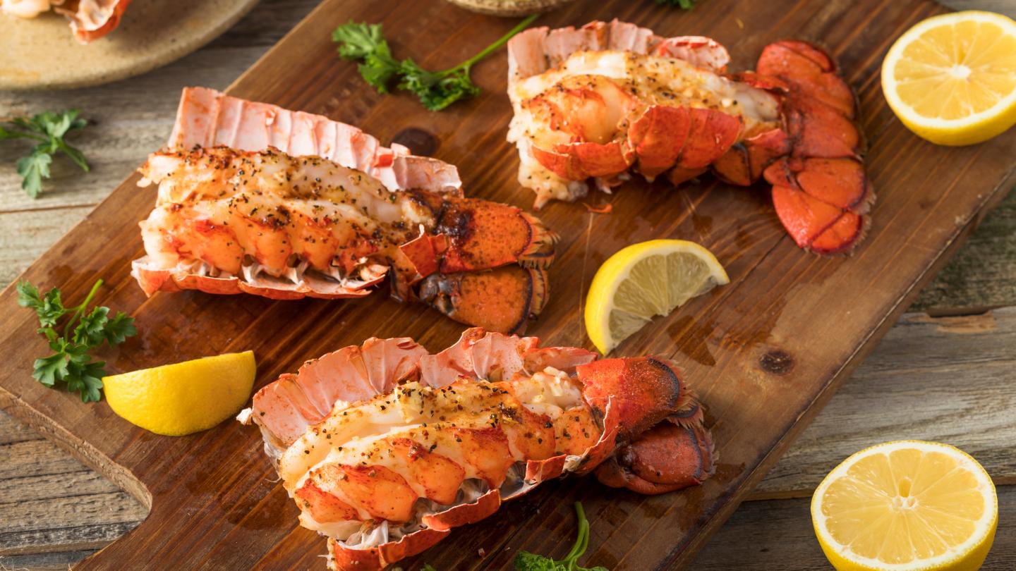 Grilled lobster tails with lemon wedges and parsley on a wooden board.