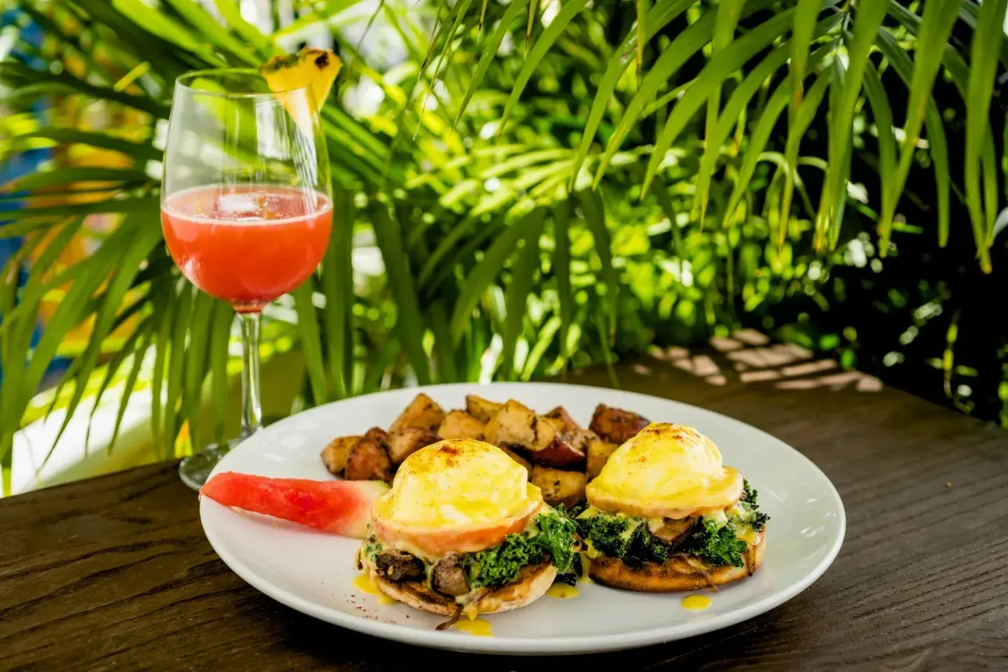 Brunch with eggs Benedict, potatoes, watermelon, and a tropical drink.