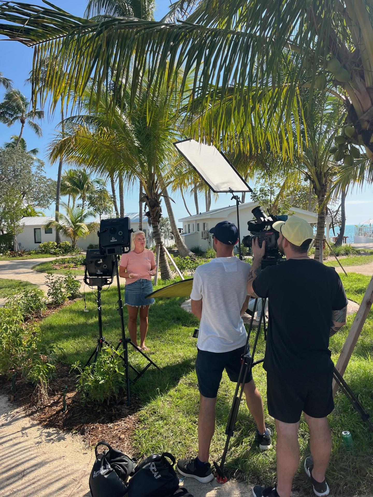 Film crew recording outdoors on a sunny day with palm trees.