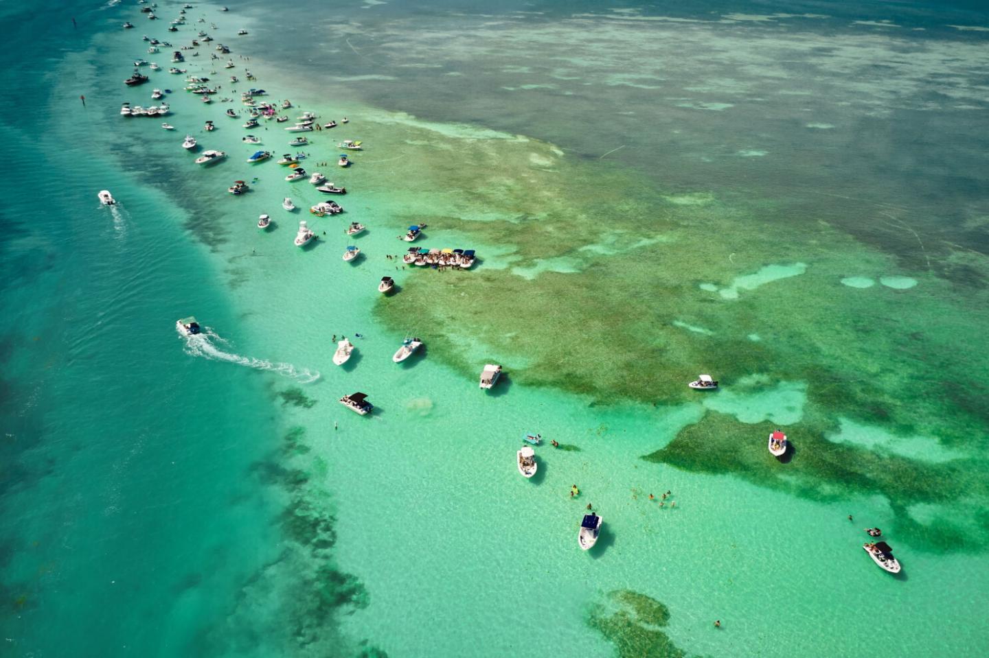 Boats scattered on turquoise water near a coral reef.