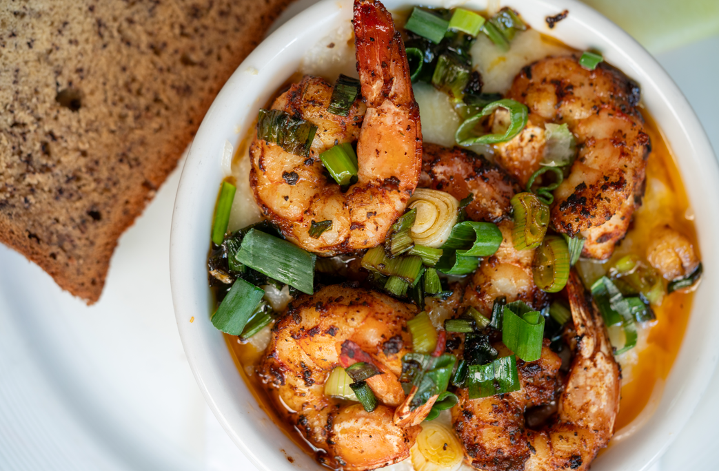 Spicy shrimp with green onions in a bowl beside a slice of toasted bread.