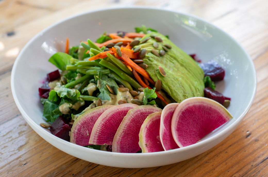 Salad with avocado, watermelon radish, carrots, and greens on a wooden table.