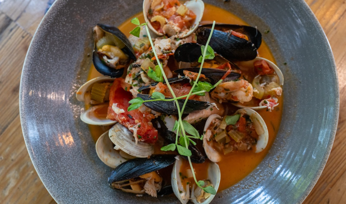 Seafood stew with mussels, clams, and shrimp in a gray bowl, garnished with herbs.