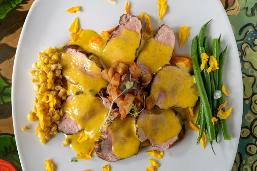 Sliced meat with yellow sauce, corn, beans, and garnish on a white plate.