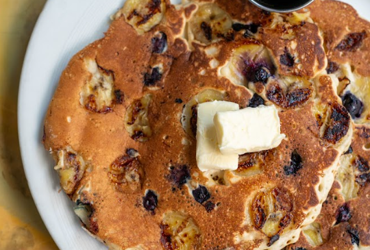 Pancakes with blueberries, bananas, and a butter pat on a white plate.