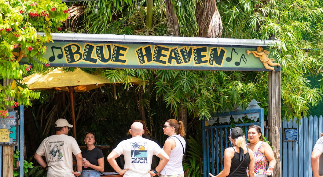 People gathered under a sign reading "Blue Heaven" with lush greenery around.
