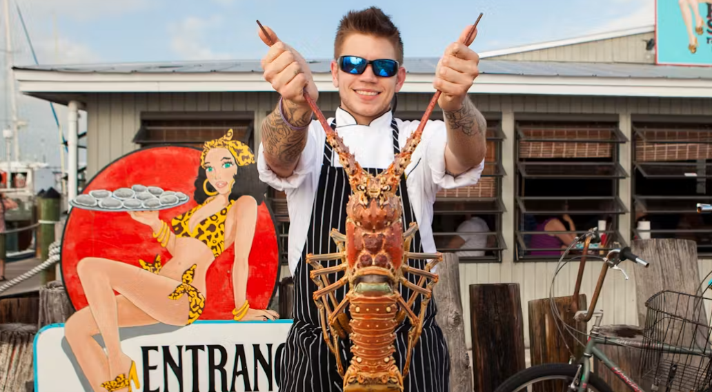Man smiling, holding a lobster in front of a seafood restaurant.