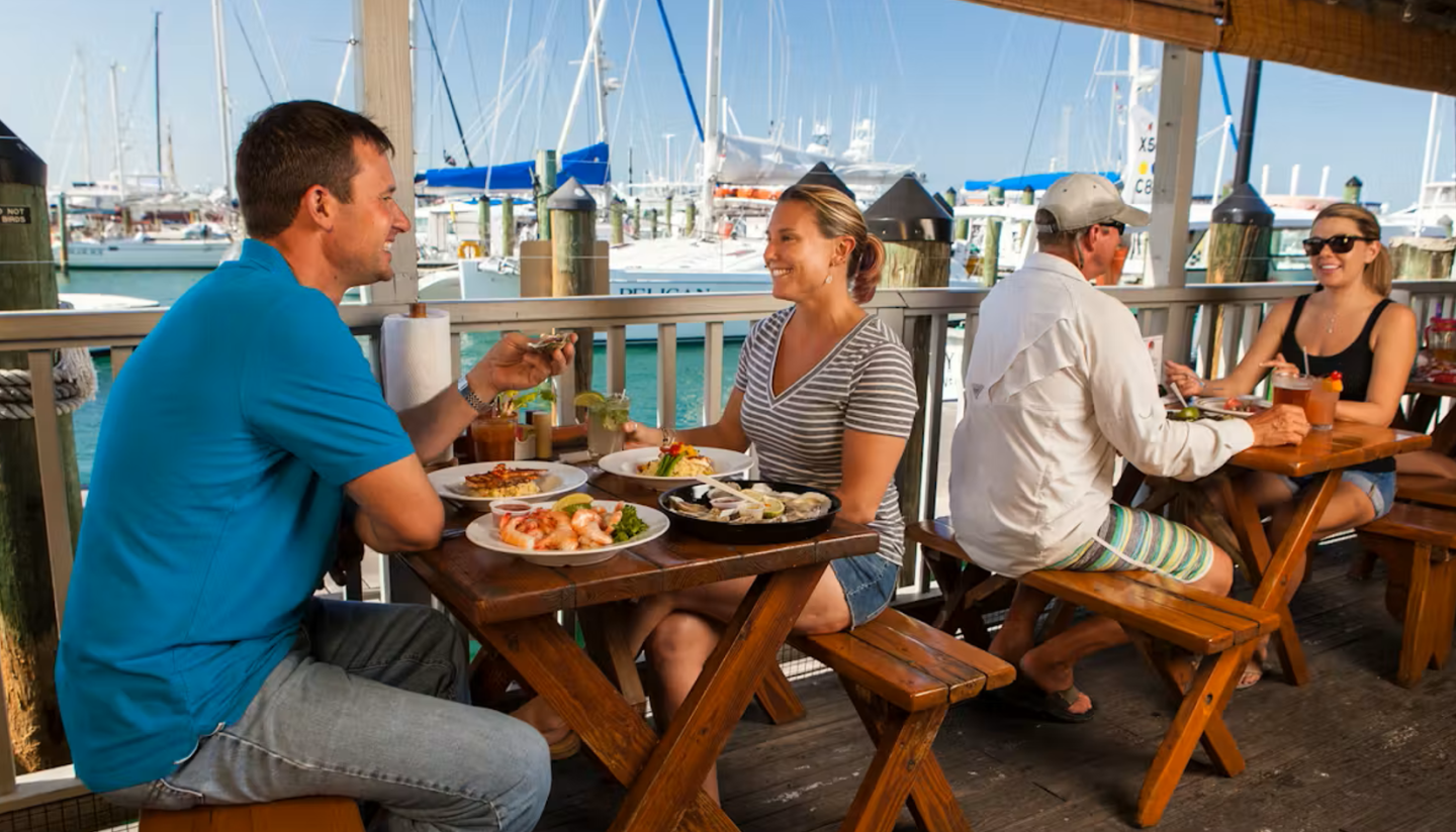 Outdoor dining by the marina with two couples enjoying meals.