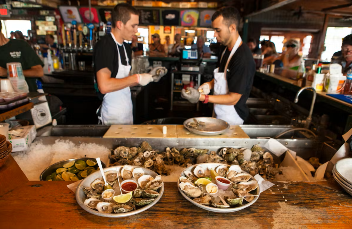 Two chefs shucking oysters at a busy seafood bar.