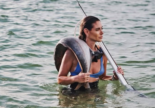 Woman in water holding a large fish over her shoulders.