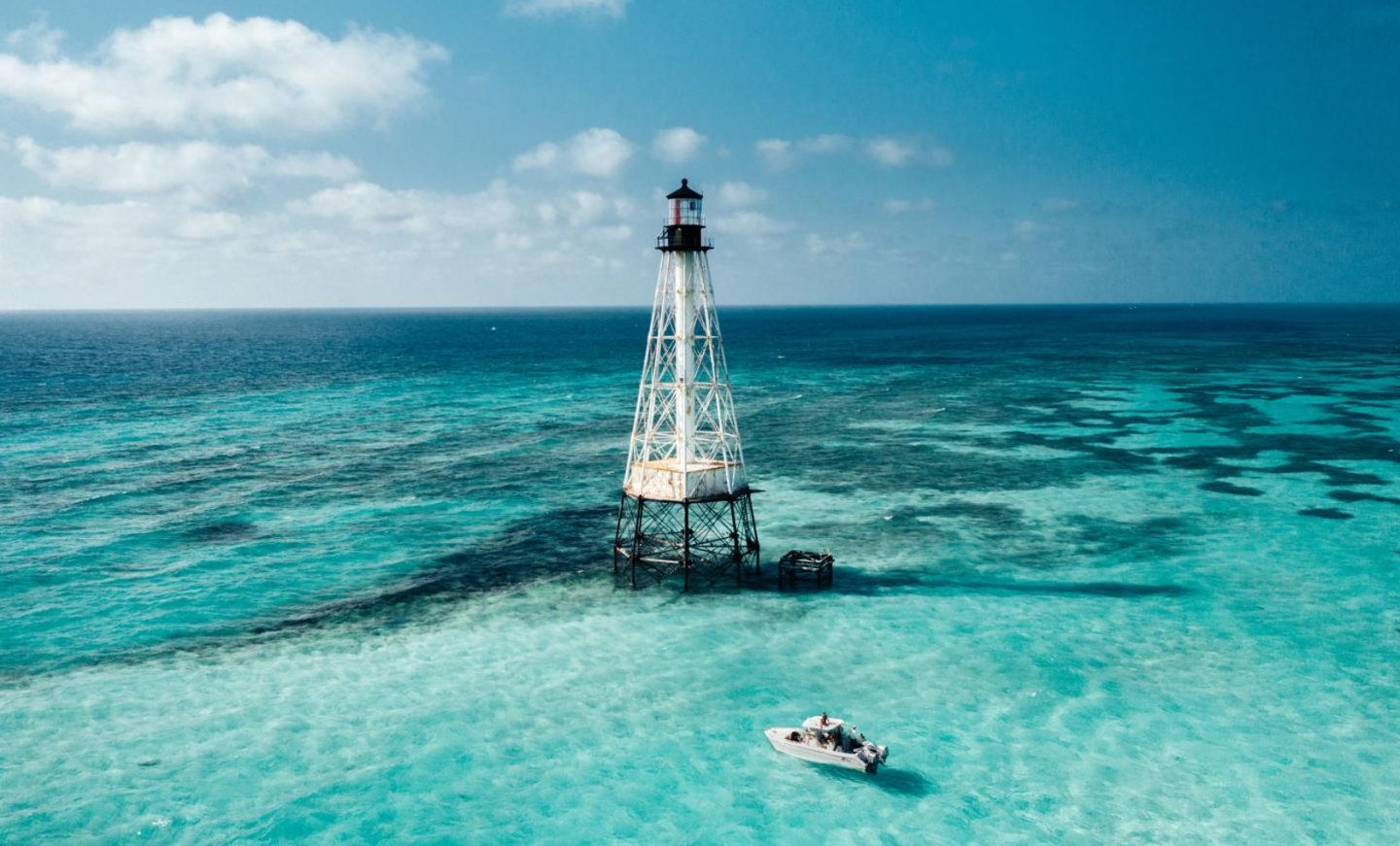 Lighthouse and boat on clear turquoise ocean under a blue sky.