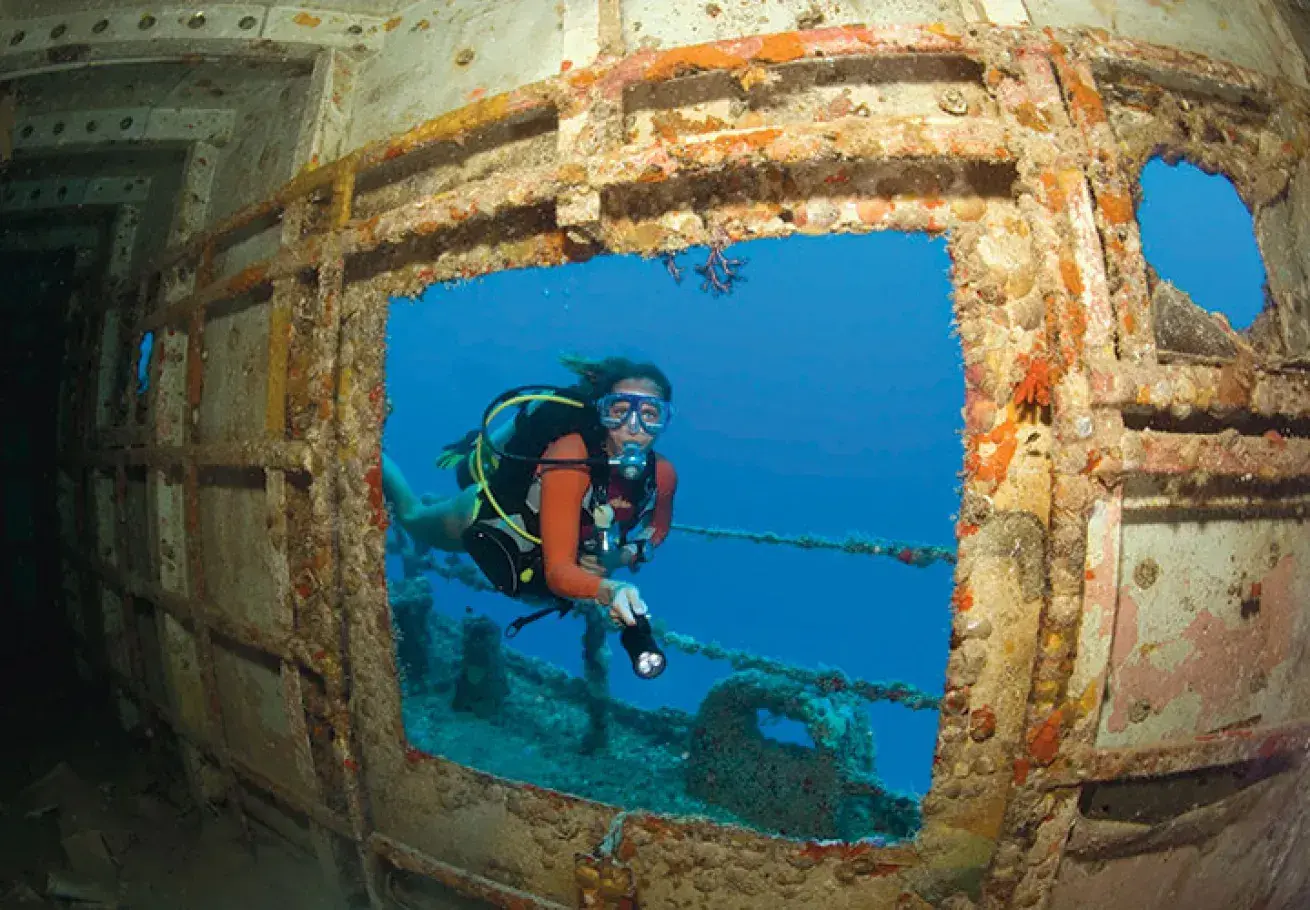 Diver exploring a sunken shipwreck underwater.
