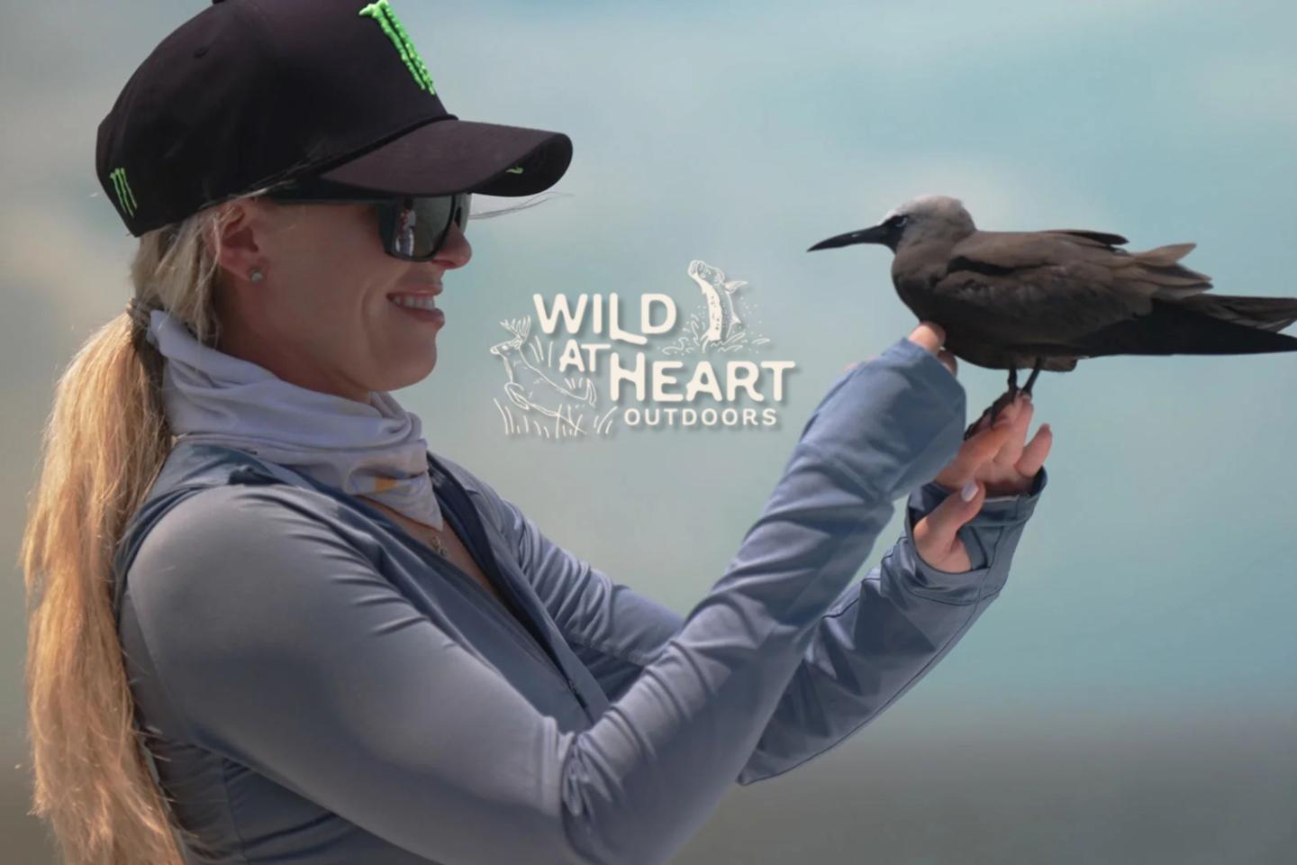 Woman in sunglasses holding a bird outdoors, with text "Wild at Heart" behind.