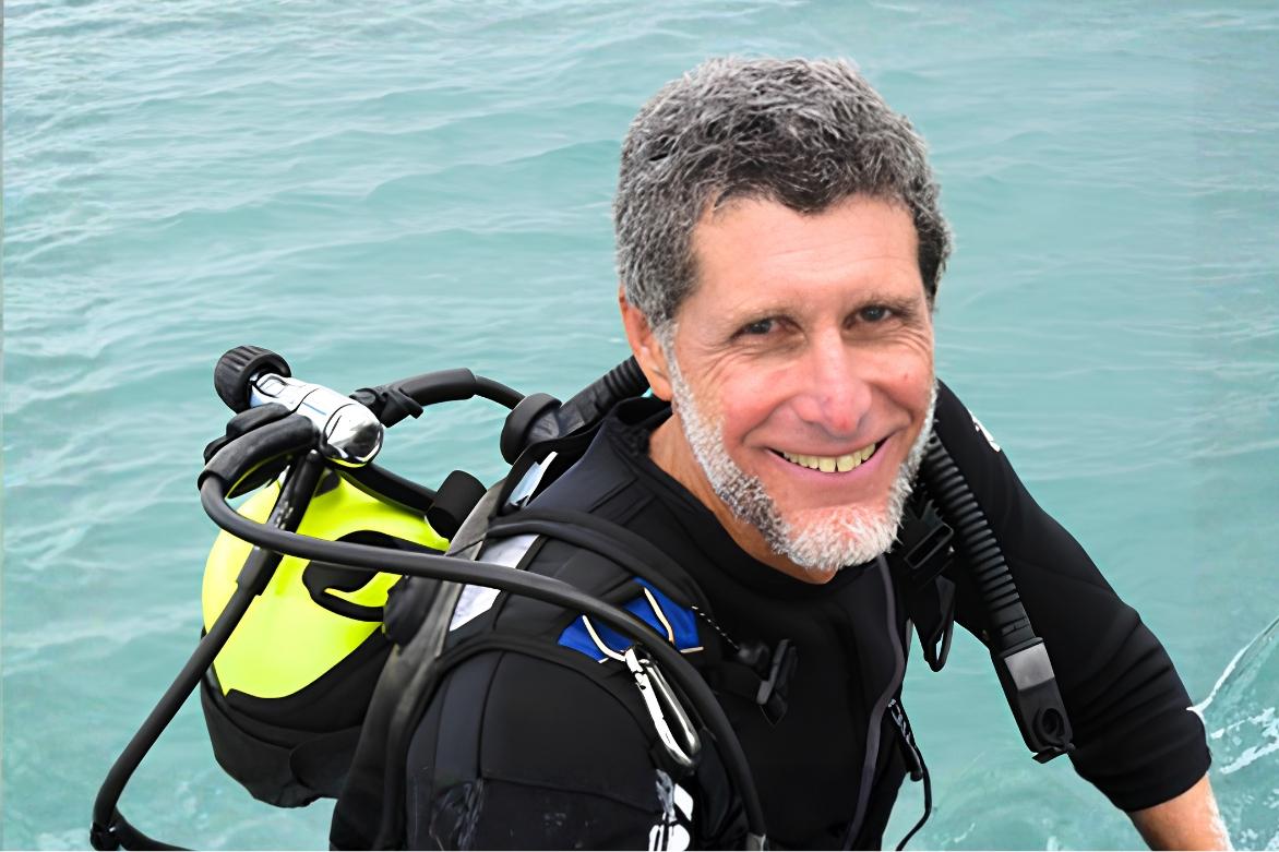 Man in scuba gear smiling by the ocean.