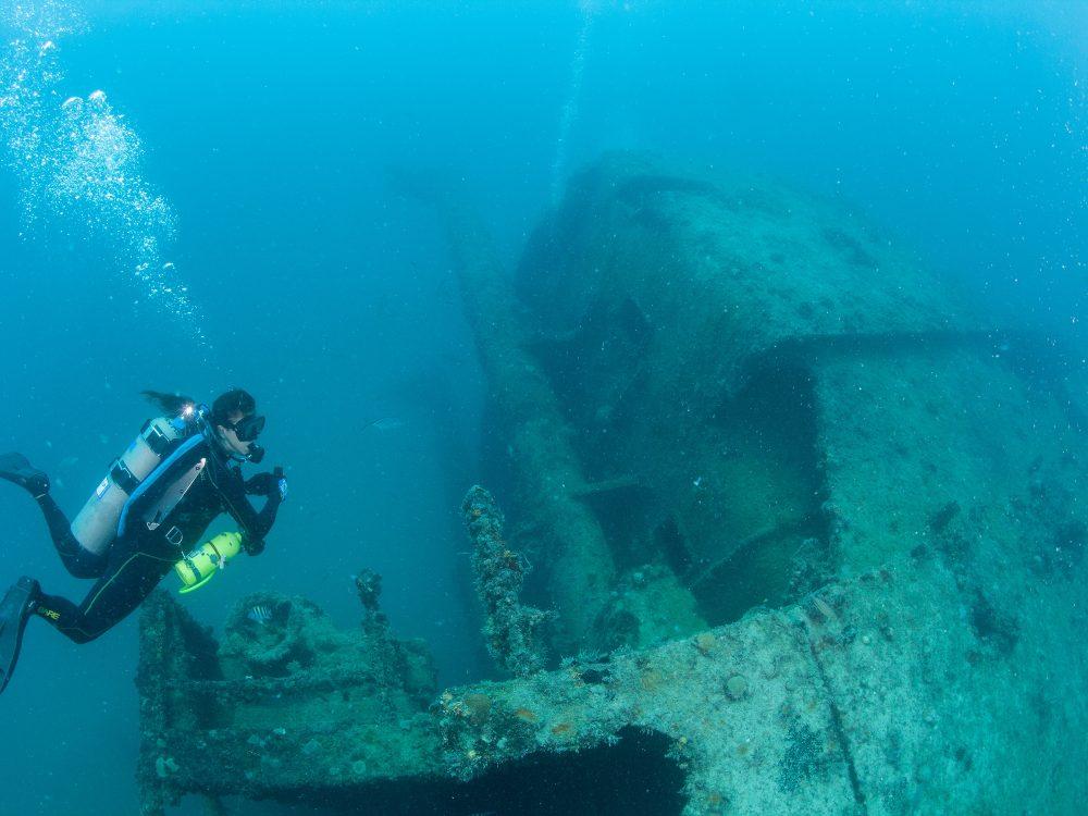 Diver exploring a sunken shipwreck under clear blue waters.