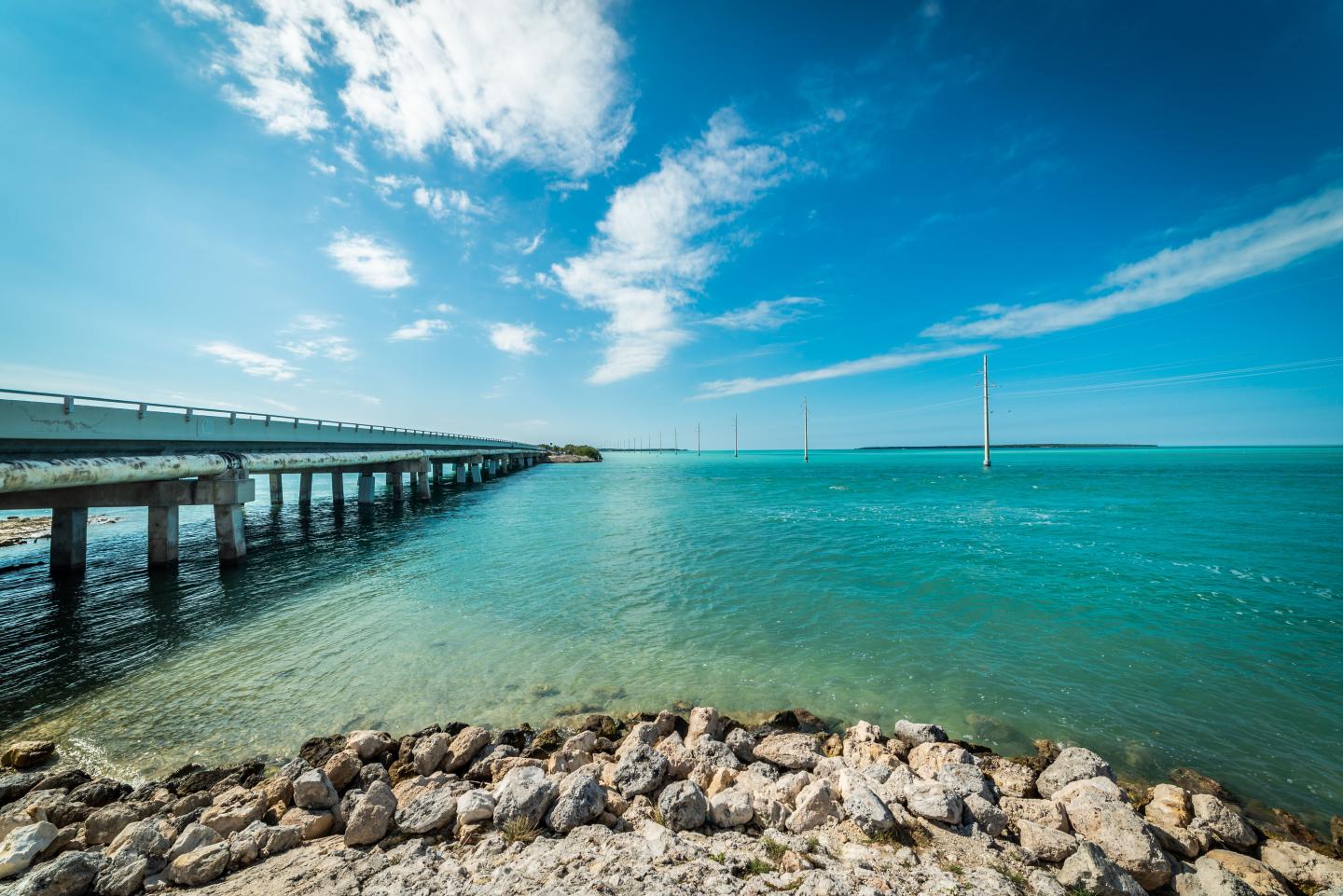 Bridge extending over calm turquoise water under a clear blue sky.