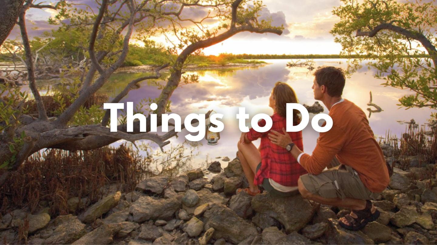 Couple sitting on rocks, admiring a sunset over a tranquil lake.