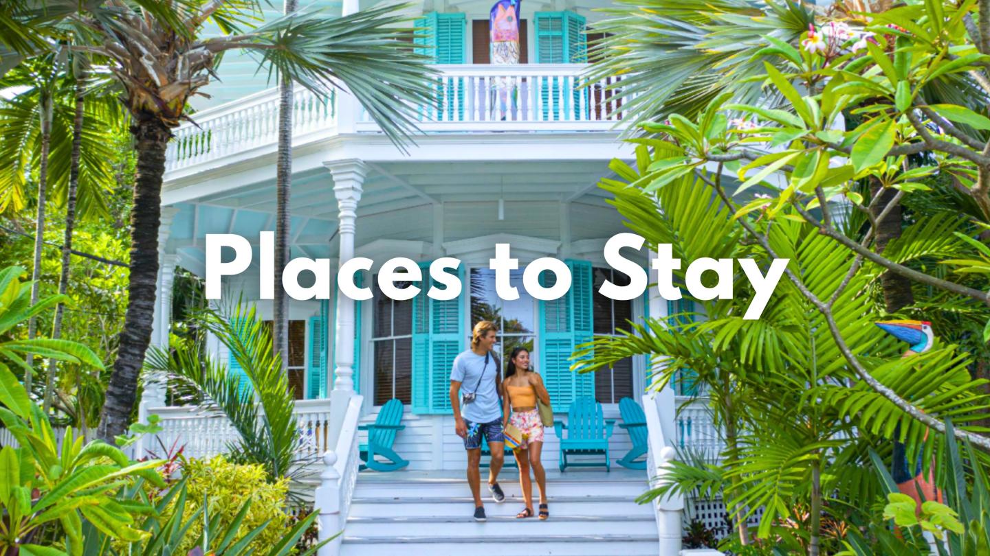Couple on steps of a tropical blue house surrounded by lush greenery.