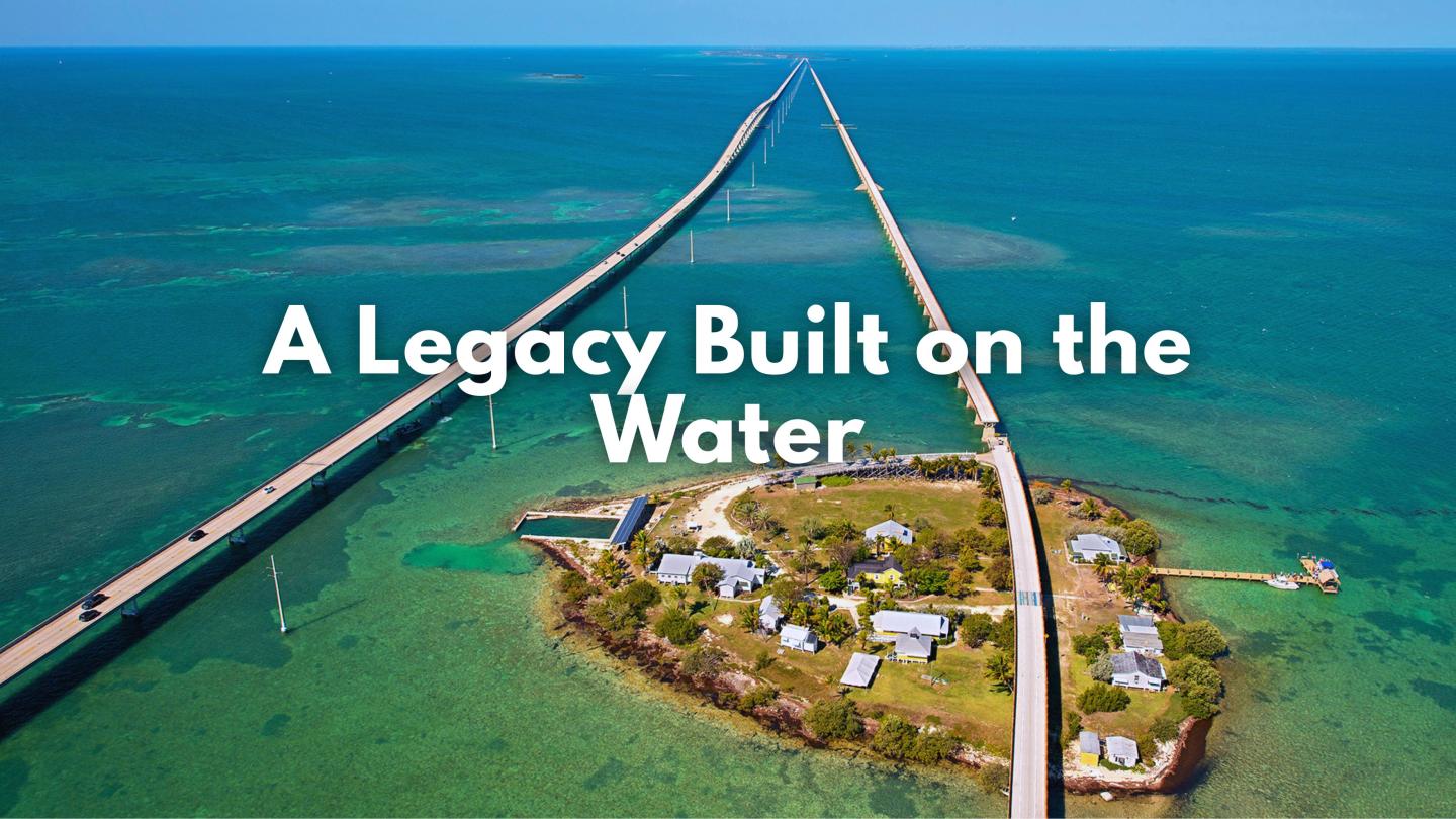 Bridge extending over blue water, small island with buildings below.