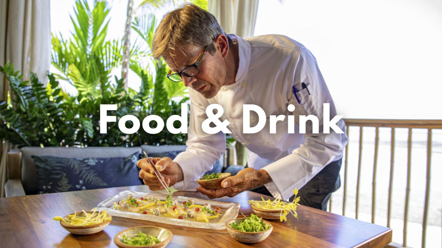 Chef plating food in a bright, plant-filled dining area.