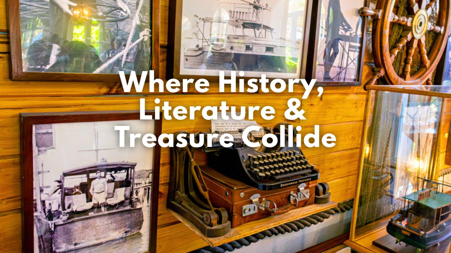 Antique typewriter on a shelf with framed photos and a ship wheel nearby.
