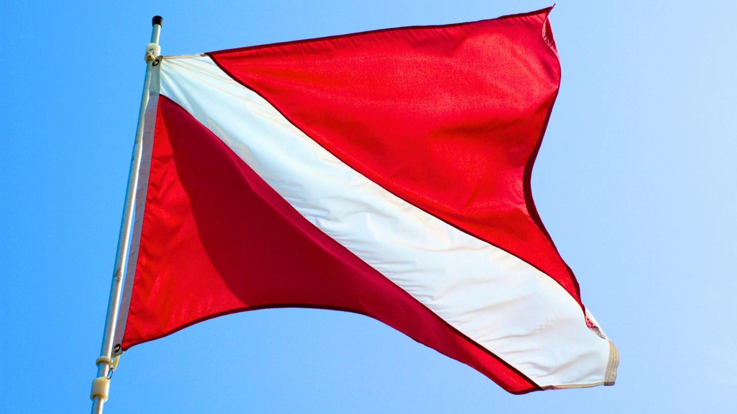Red diving flag with white diagonal stripe against blue sky.