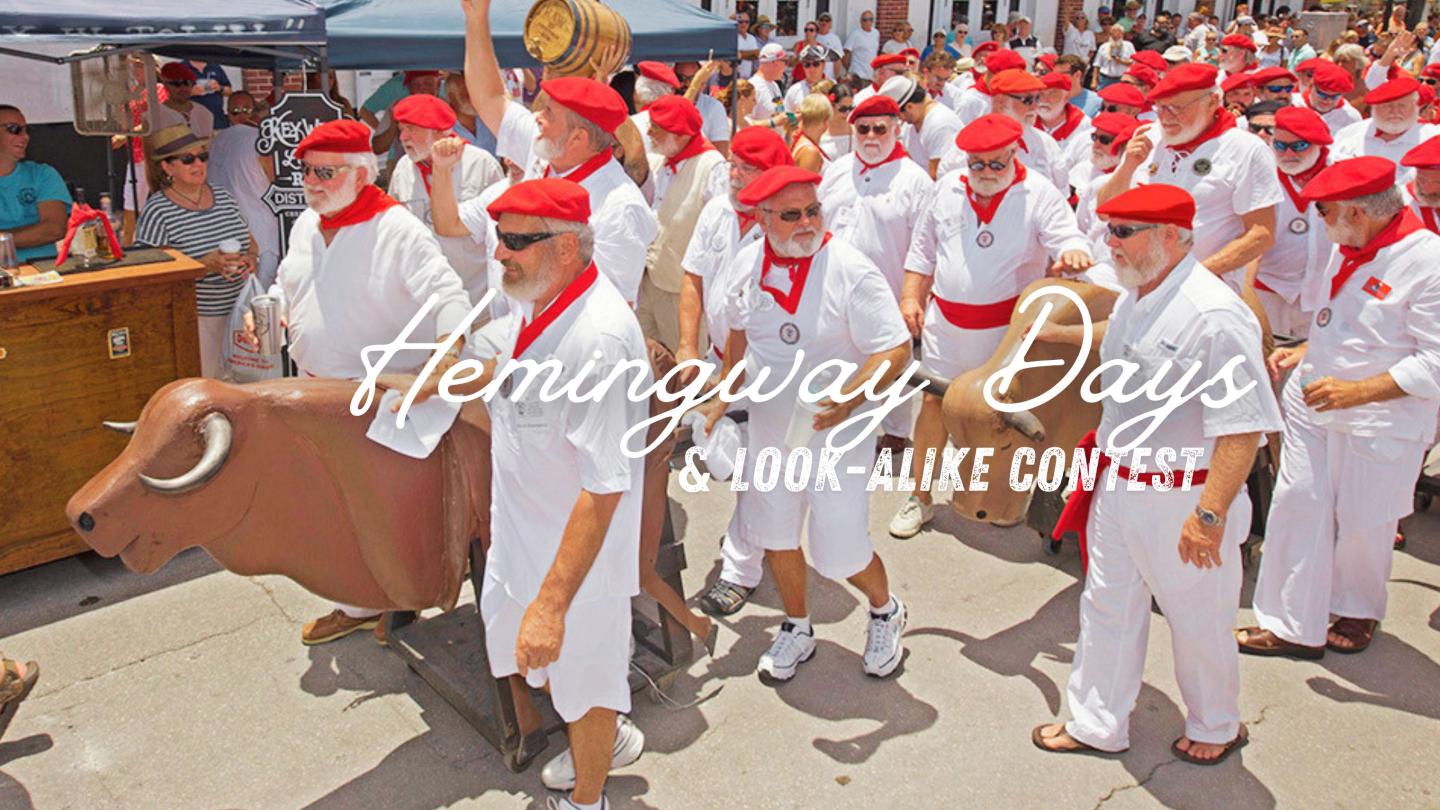 Men in white with red berets and scarves walk with fake bulls at a festival.