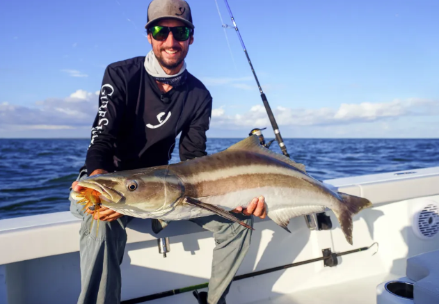 Man happily holding large fish on a boat under a clear blue sky.