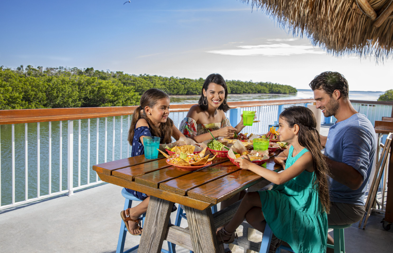 Family enjoying outdoor meal by a riverside with lush greenery.