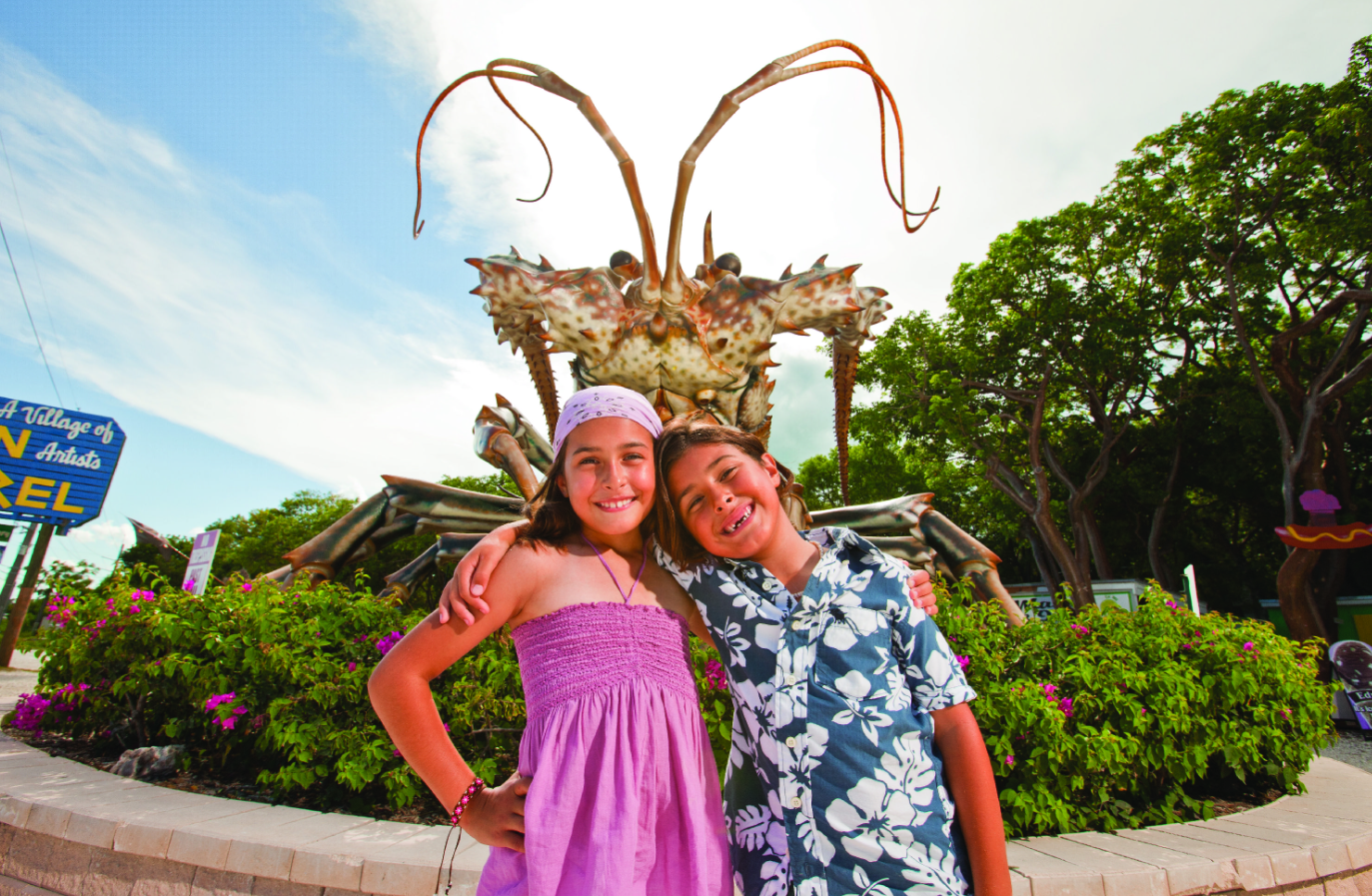 Two children smiling in front of a large lobster sculpture.