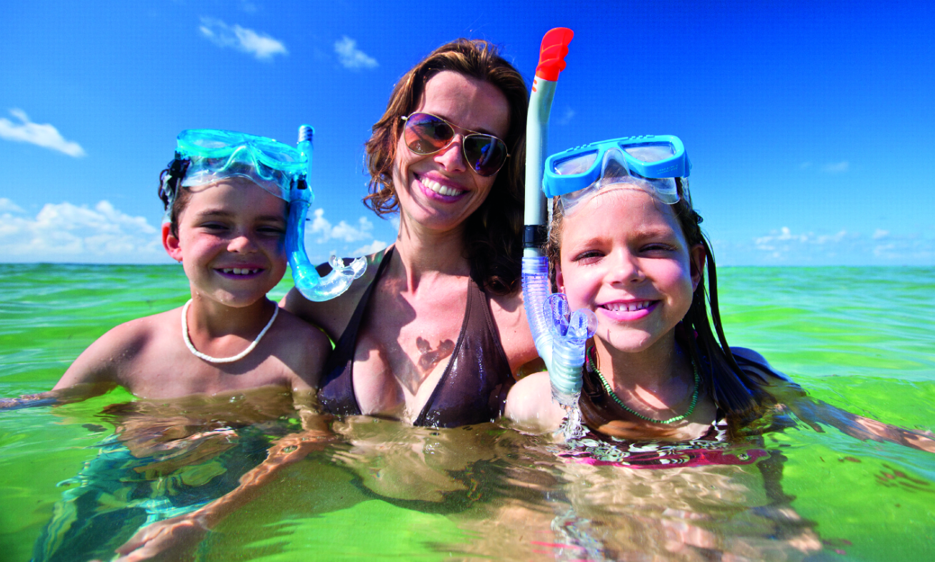 Smiling family snorkeling in clear green water.