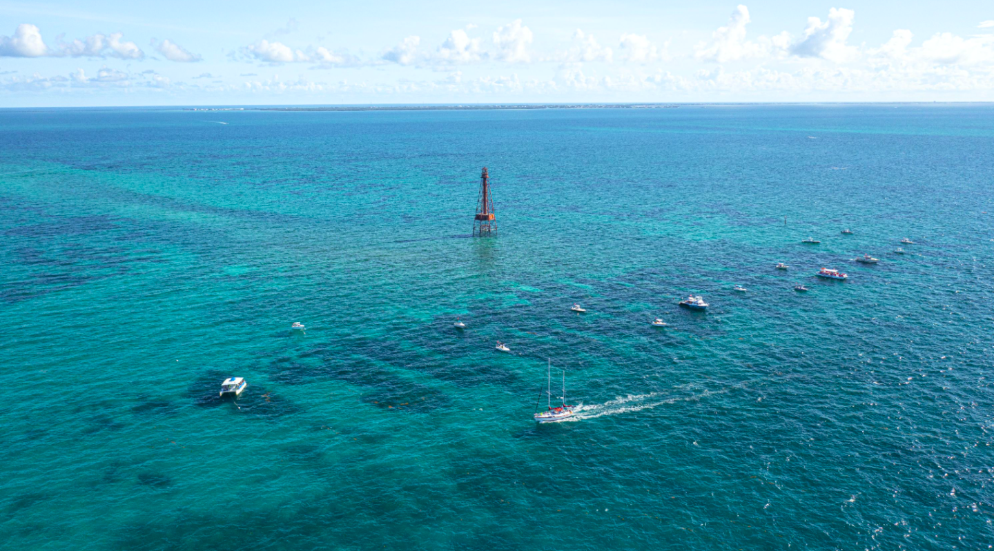 Turquoise sea with a distant lighthouse and scattered boats.