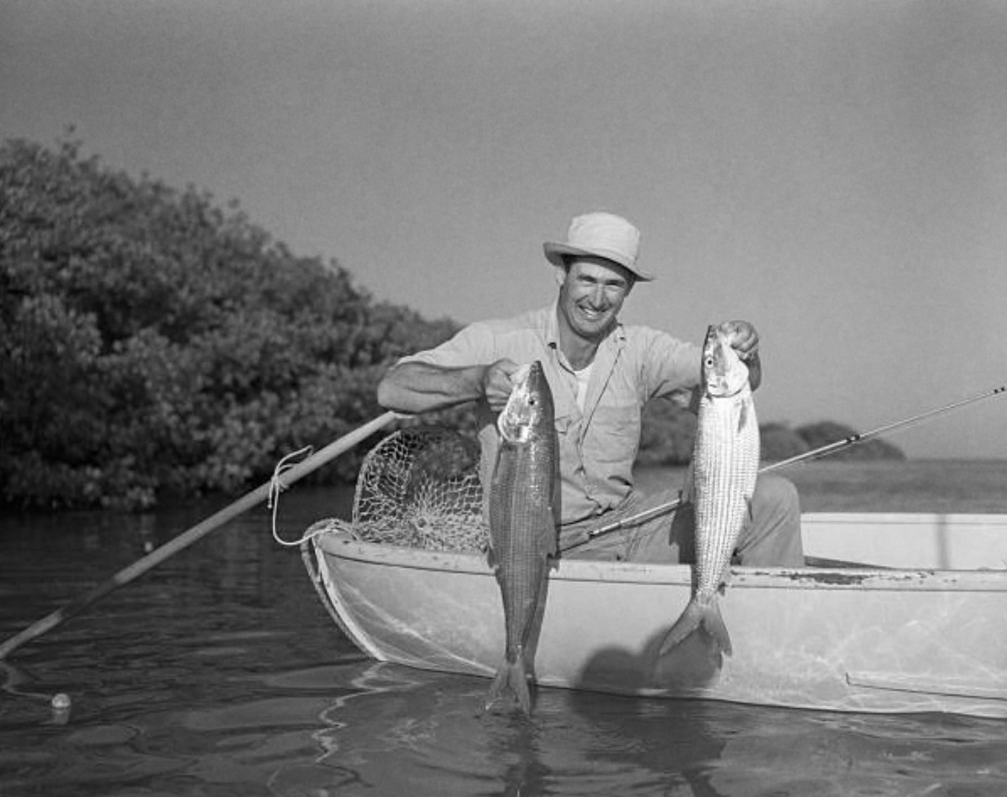 Man in a boat holding two large fish, smiling.