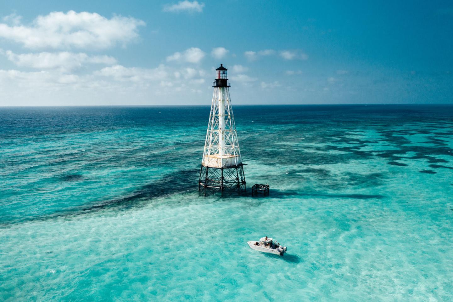 Turquoise ocean with a lighthouse and a small boat nearby.
