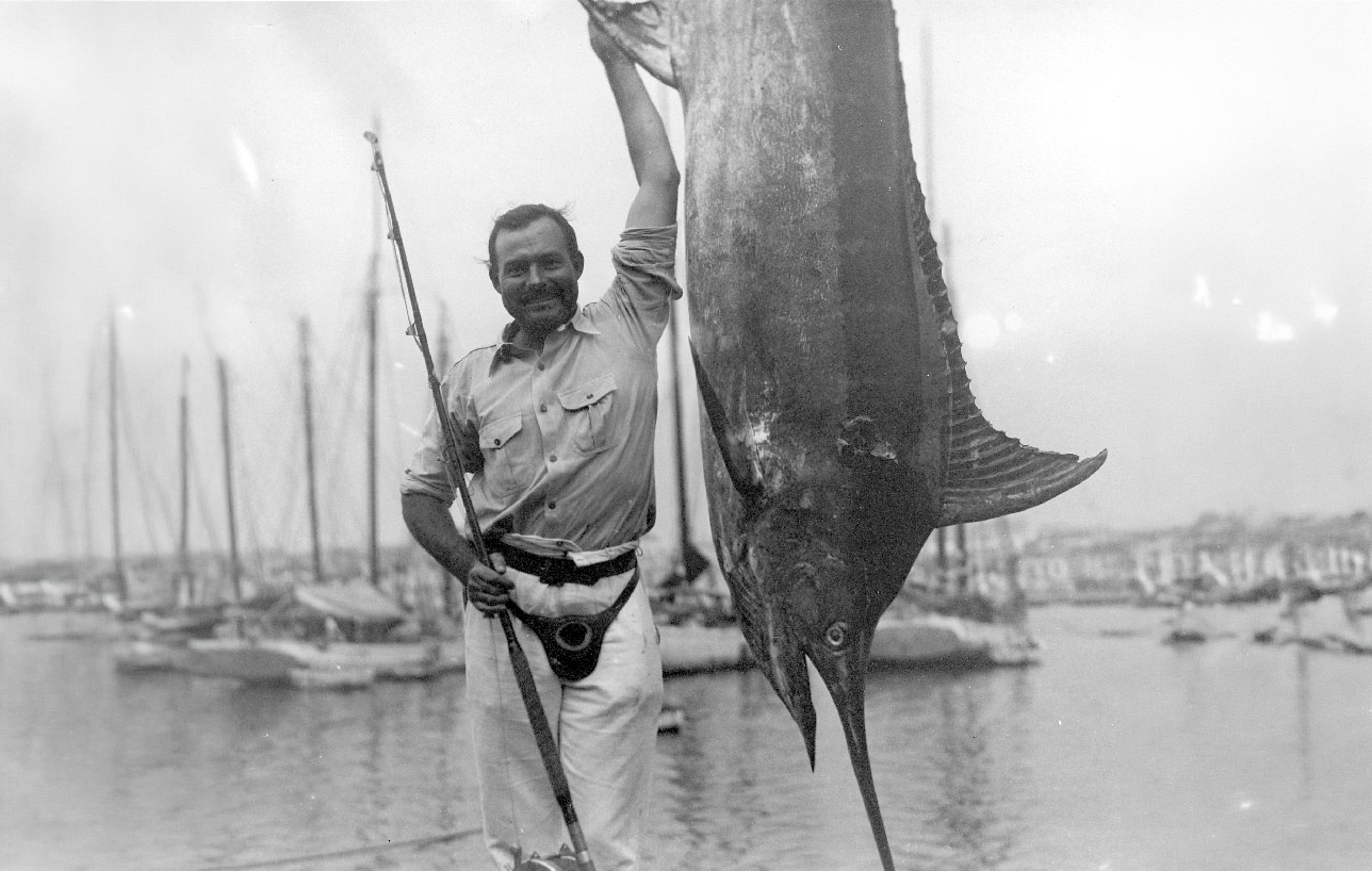 Man proudly holding a large fish by the harbor.