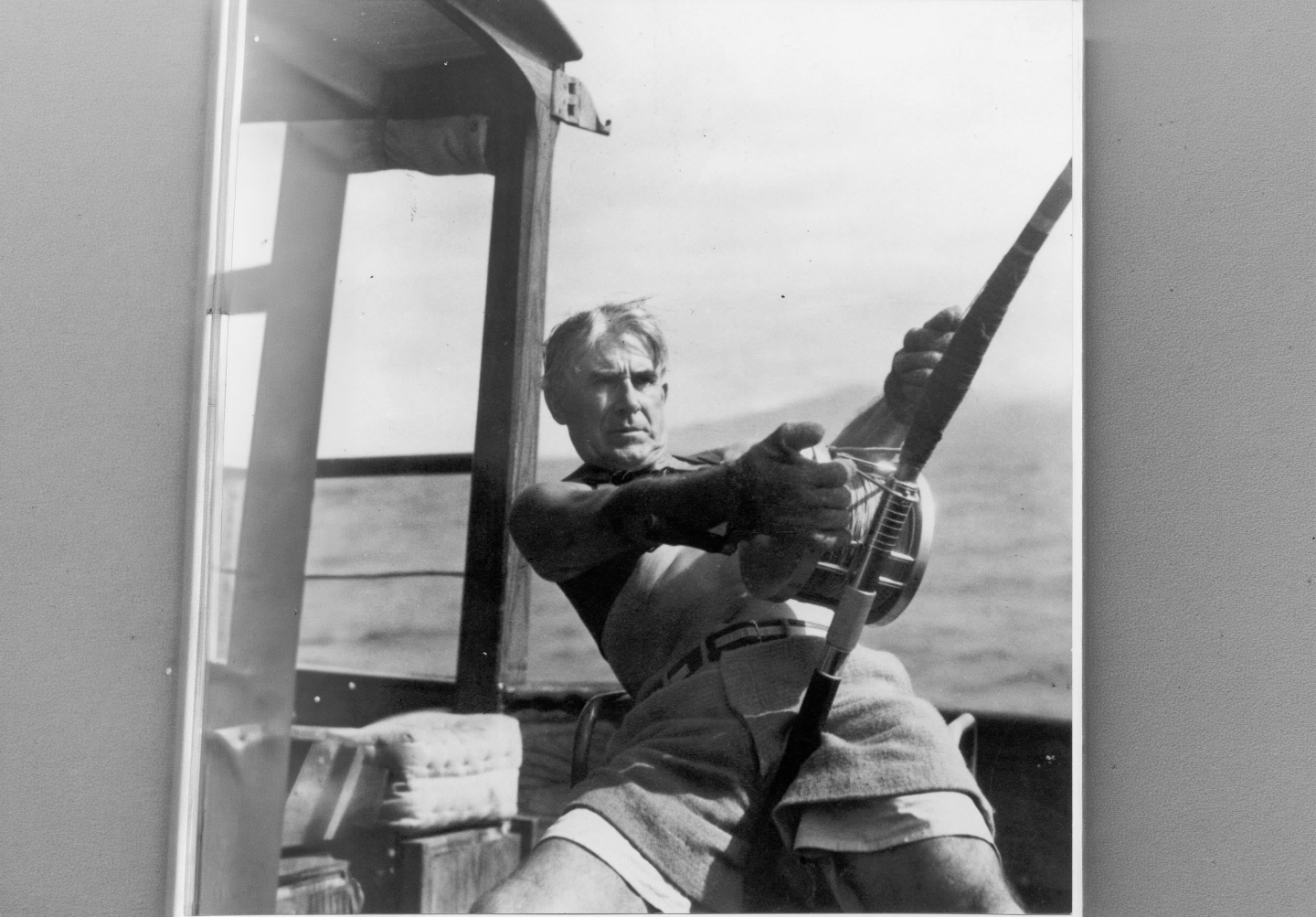 Man on a boat struggling with large fishing rod, ocean in the background.