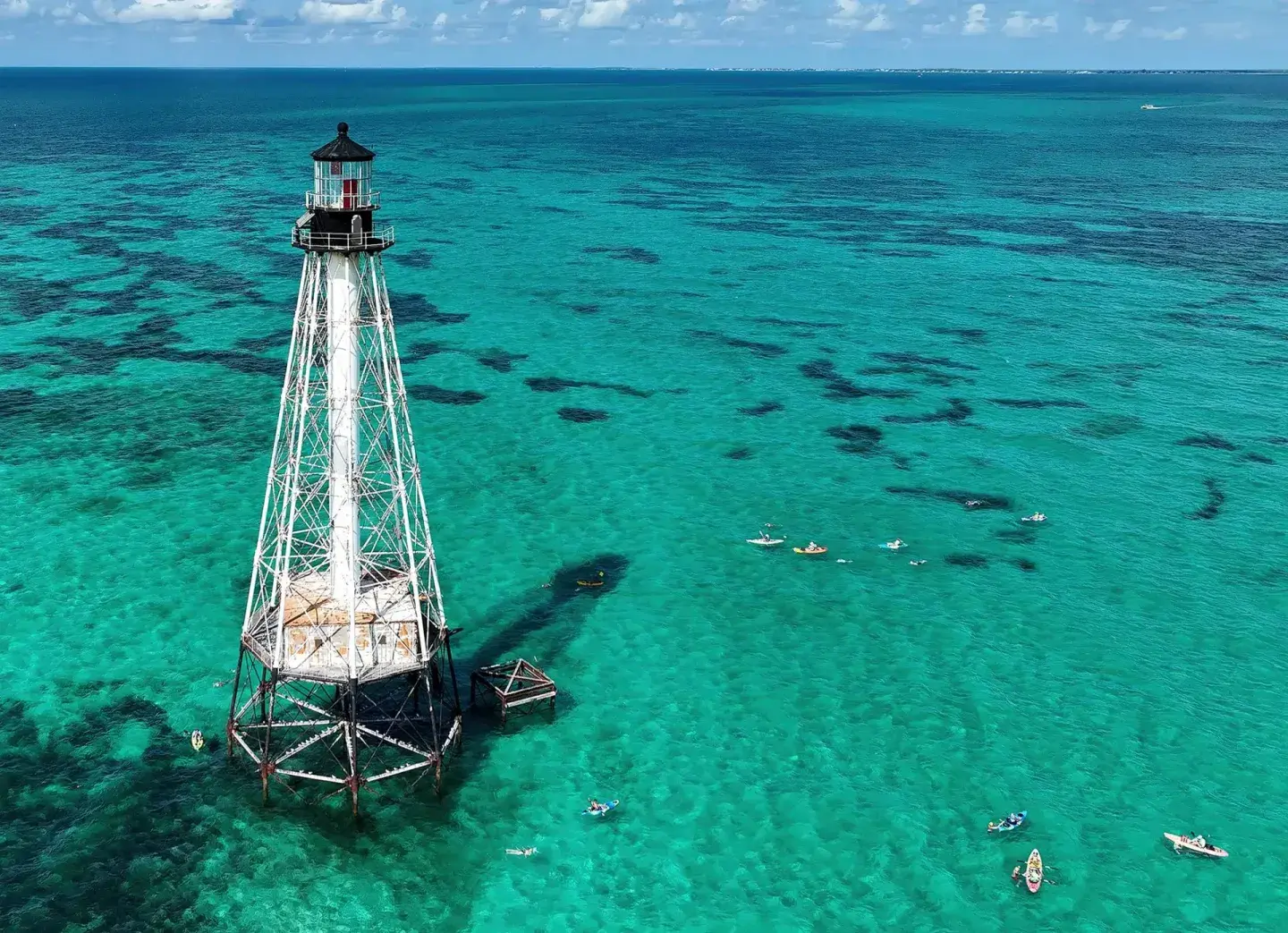 Lighthouse tower stands in clear turquoise ocean water.