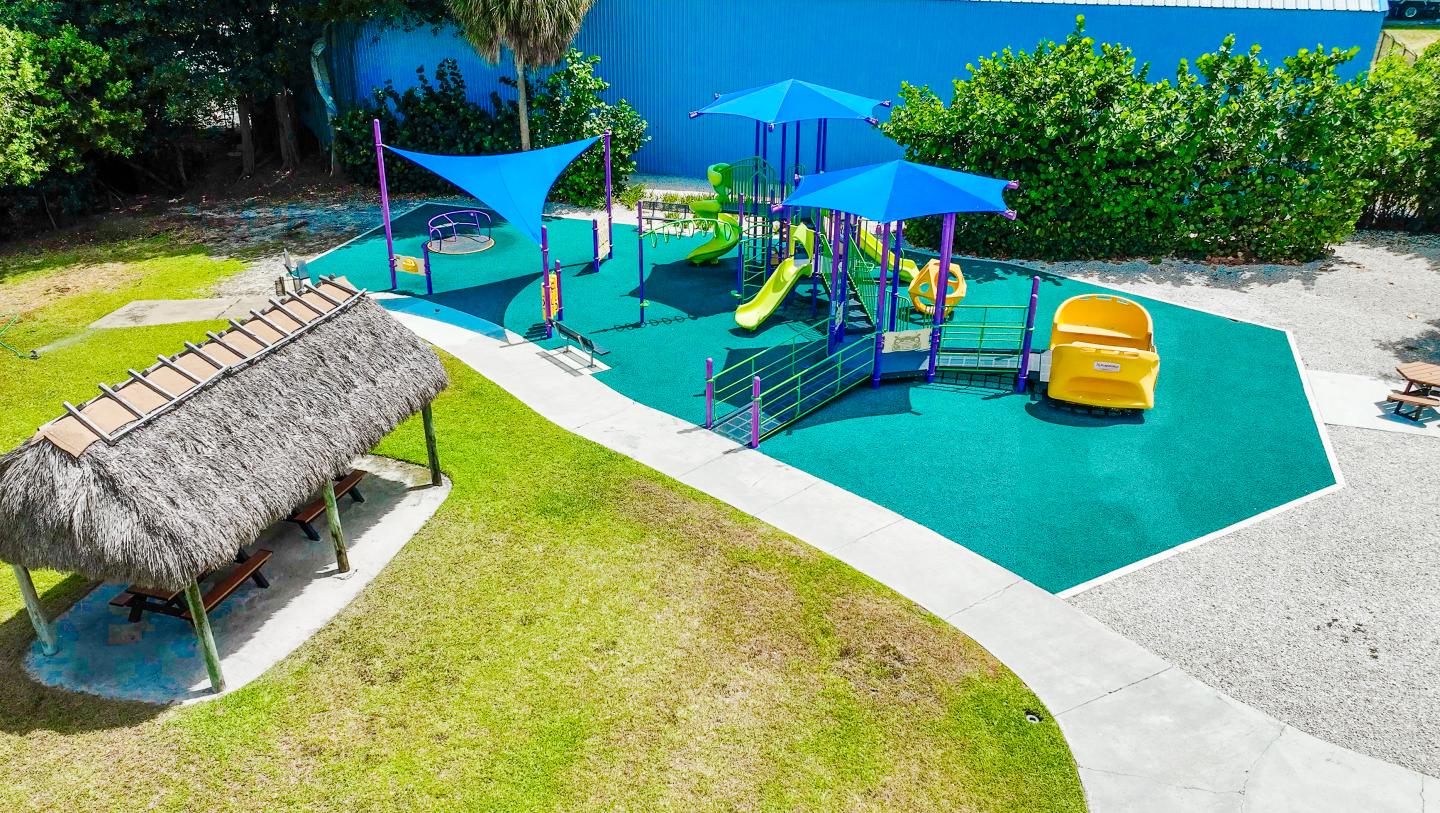 Playground with blue slides, yellow seesaw, and shaded huts.