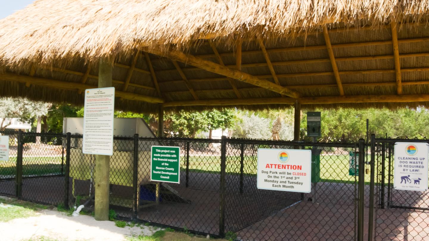 Fenced-in area with signs under a thatched roof.