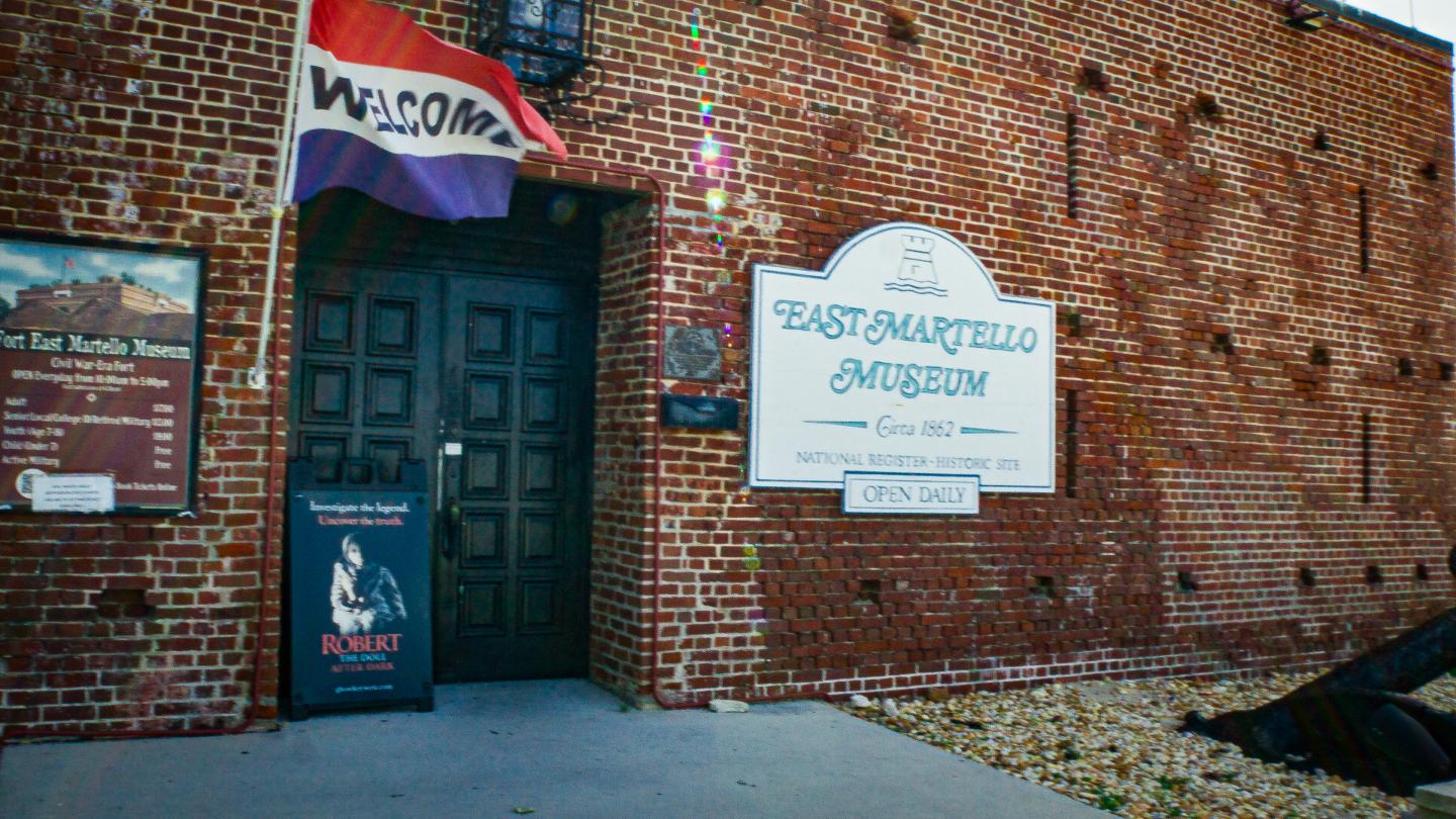 Red brick building entrance with signs and a rainbow flag.