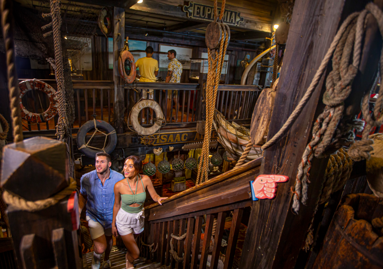 Rustic staircase in a wooden ship-themed interior with two people ascending.
