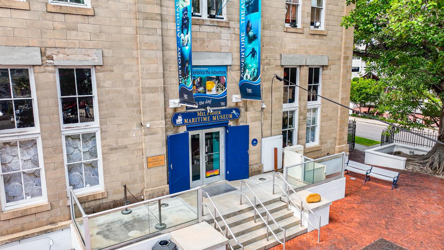 Historic building entrance with banners, steps, and a tree on the right.