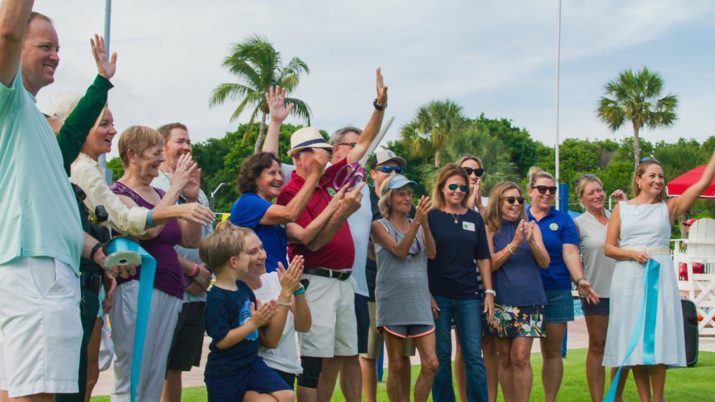 Group of people outdoors, smiling and raising hands, with palm trees in the background.