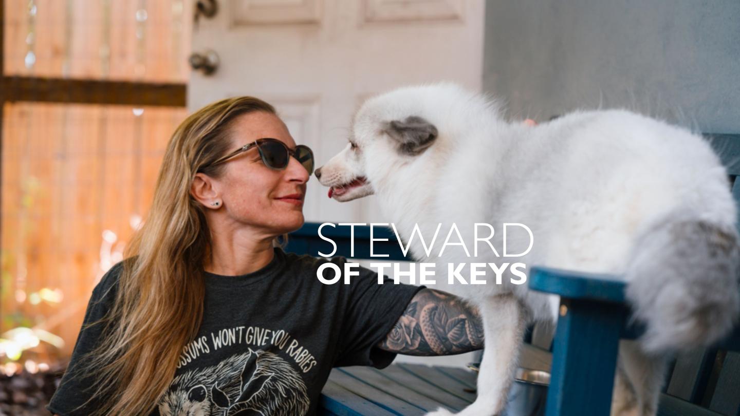 Woman with sunglasses sitting beside a fluffy white dog on a bench.
