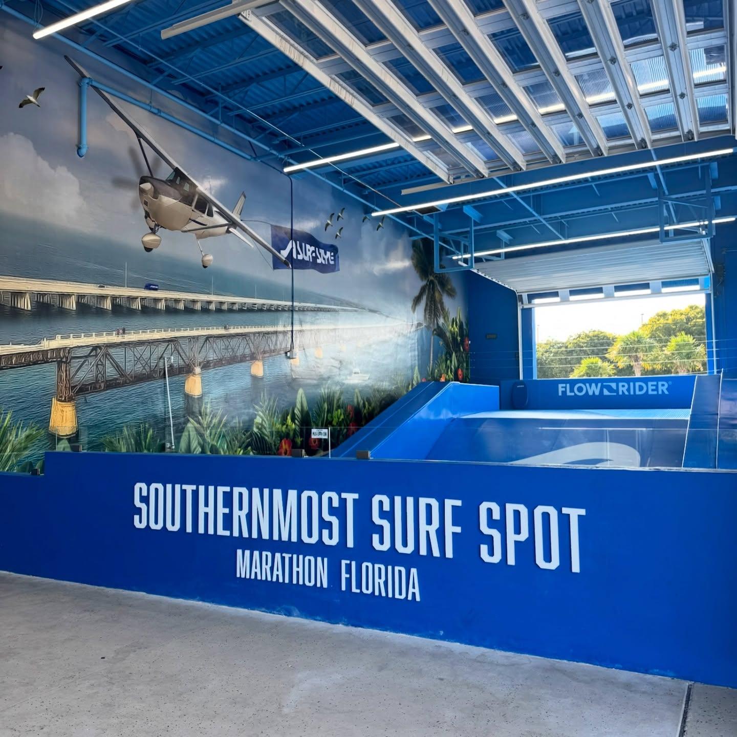 Indoor surf simulator with vibrant beach mural and blue accents.