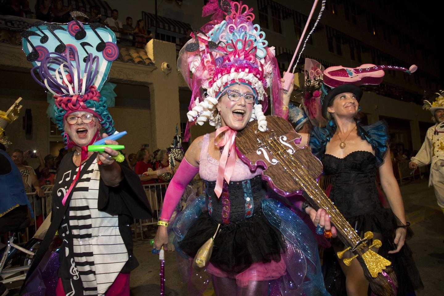Three women in colorful feathered carnival costumes at night.
