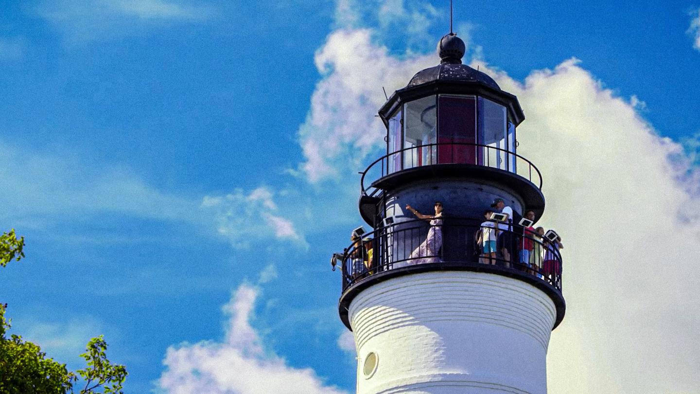 White lighthouse with black railing against a blue sky and clouds.