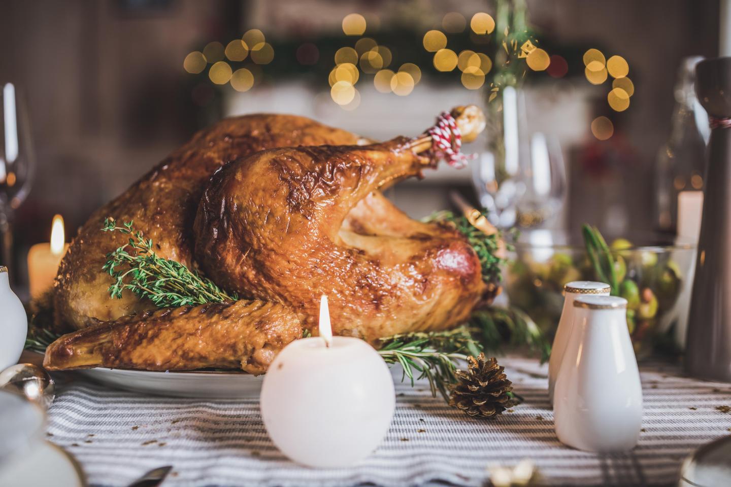 Roasted turkey on a platter with herbs and candles on a festive table.